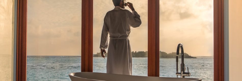 man standing in bathroom with bathtub next to body of water